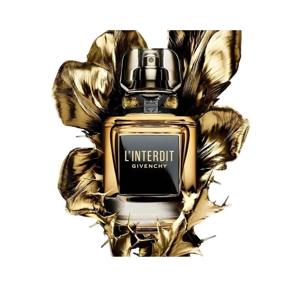 Flacon de parfum avec étiquette noire et liquide doré. Inscription L'INTERDIT et GIVENCHY. Entouré de feuilles dorées.