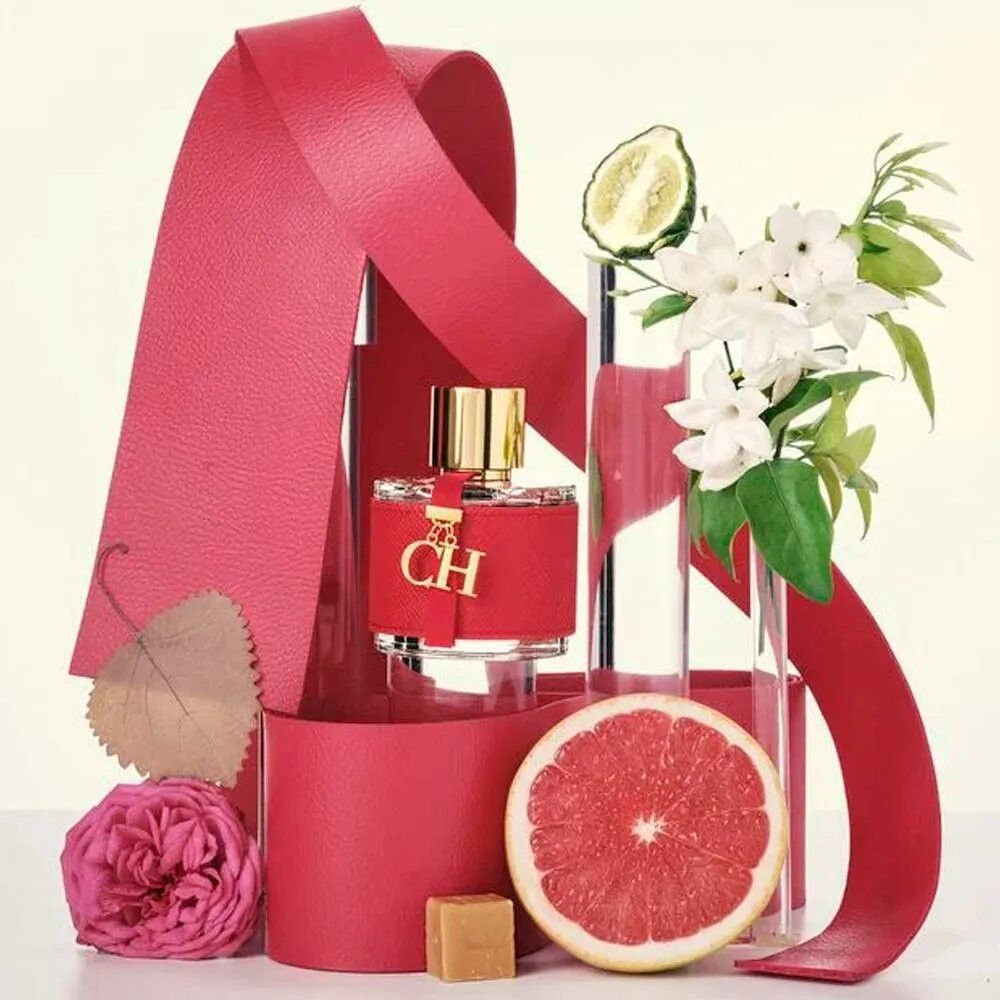 Flacon rouge avec bouchon doré et breloque. Décoration avec rubans rouges, fleurs, pamplemousse et citron vert.