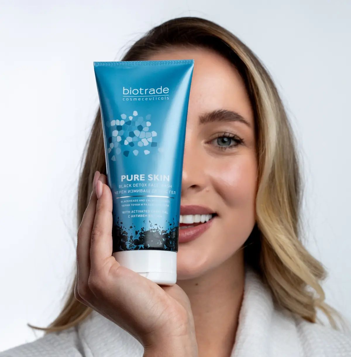 Vrouw houdt blauwe tube voor haar gezicht. Opschrift: Biotrade, Pure Skin Black Detox Face Wash.