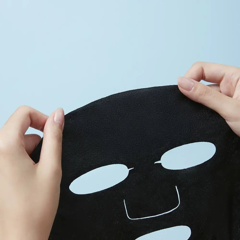 Masque facial noir avec ouvertures pour les yeux et la bouche, tenu par des mains.