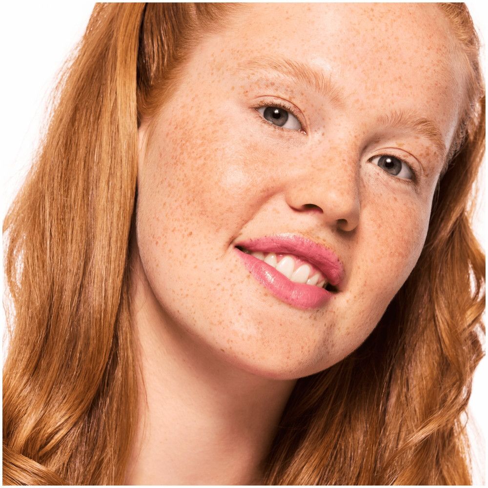 Portrait d'une femme avec des taches de rousseur et du maquillage. Elle sourit.