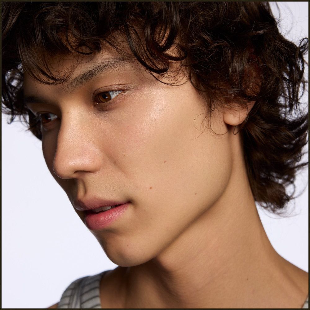 Gros plan d'un homme aux cheveux bouclés. Il regarde vers le bas. Teint clair.