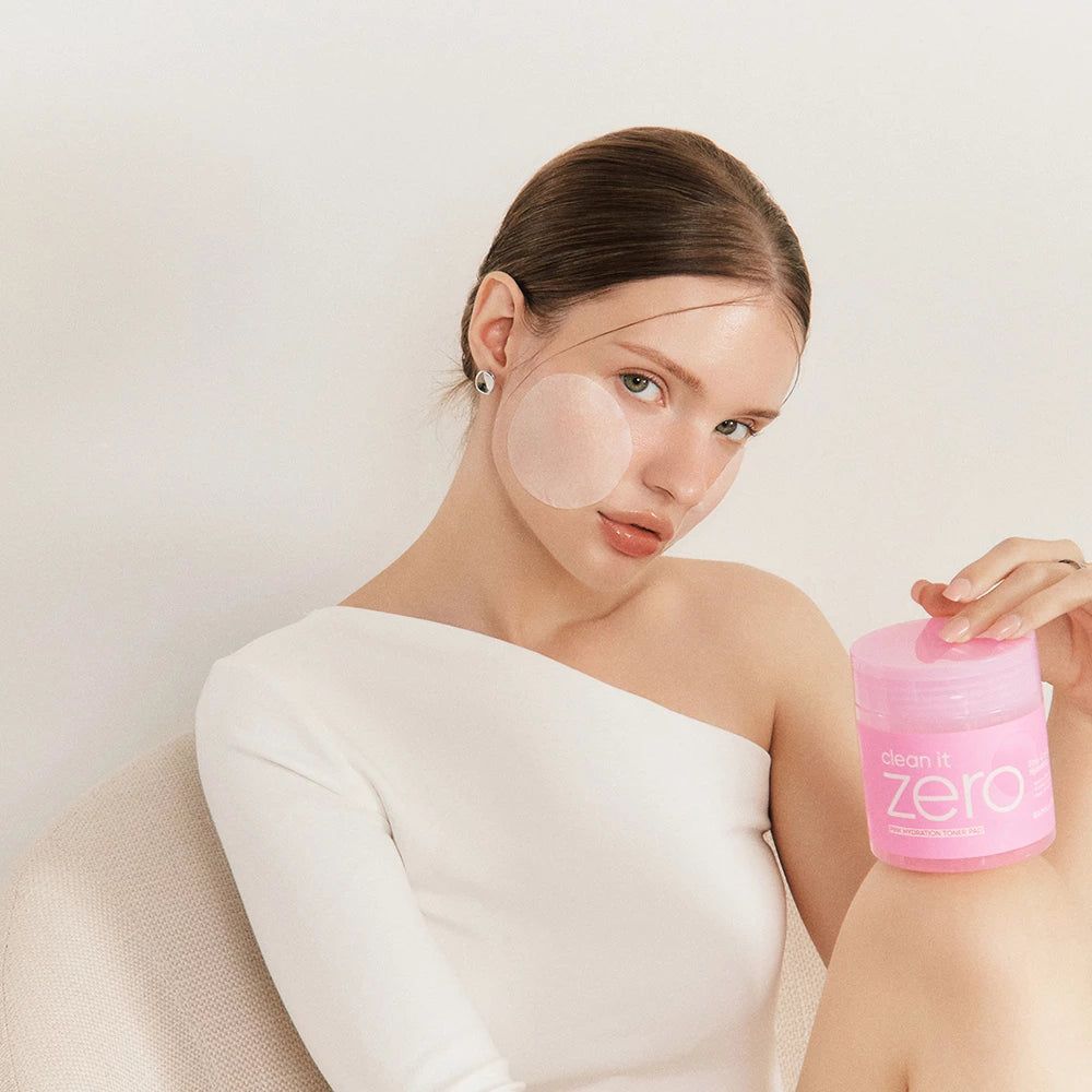 Een vrouw houdt een roze pot met "Clean it Zero" vast. Pads op haar gezicht.