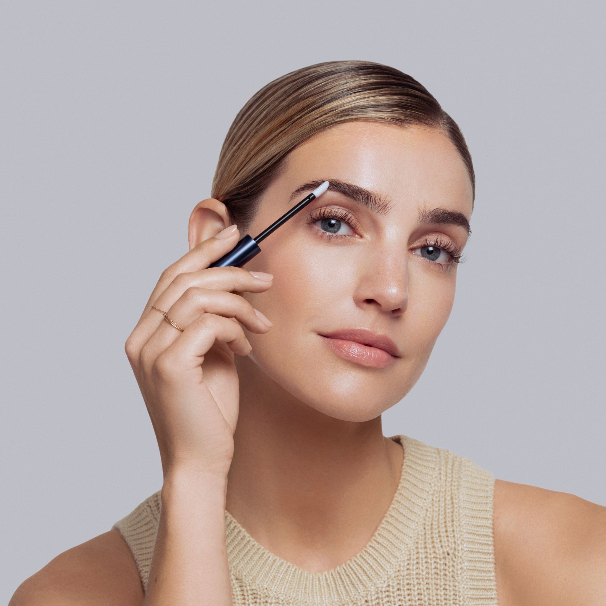 Vrouw brengt het product aan op de wenkbrauw met een applicator. Ze houdt de applicator in haar hand.