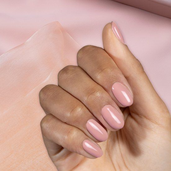 Main avec ongles vernis en N10 Rose Pompadour. Forme ovale. Sur tissu rose.