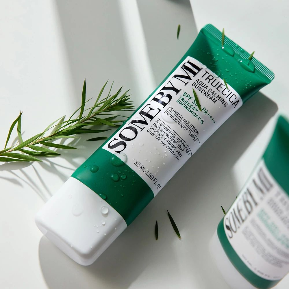 Tube de crème solaire verte et blanche. Texte : SOMEBYMI, TRUECICA Aqua Calming Suncream, SPF 50+ PA++++. Eau et feuilles.