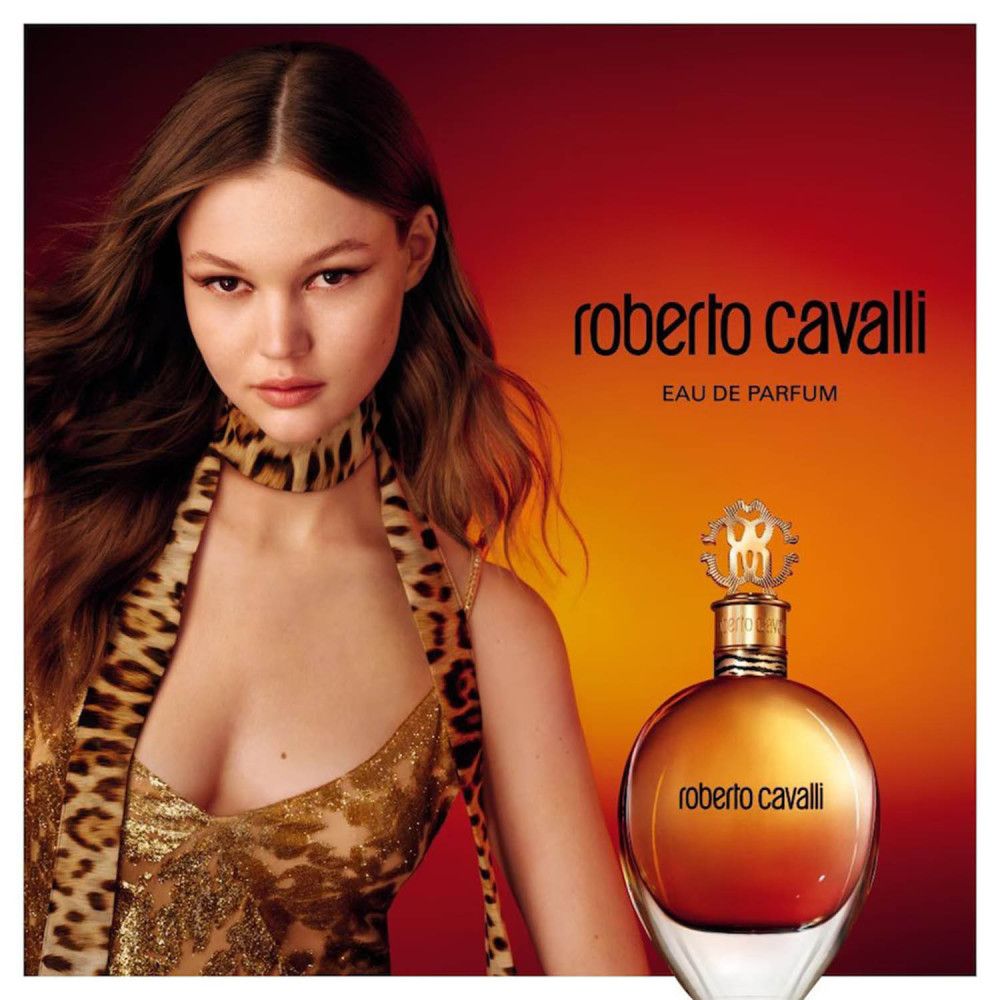 Reclamefoto met vrouw en fles. De fles is rond, met gouden dop en opschrift. Achtergrond rood-oranje.