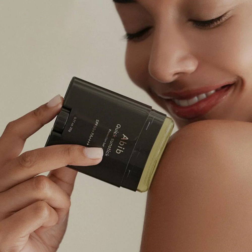 Une femme applique le ABIB Quick Sunstick Protection Bar sur son épaule.