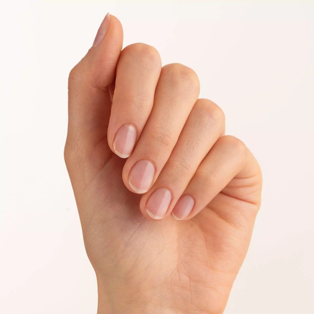 Hand met vijf gelakte nagels. Nagels zijn kort en ovaal van vorm. De nagellak is transparant.
