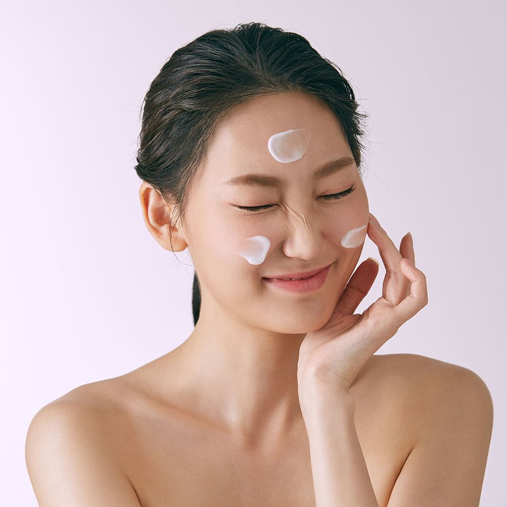 Vrouw met gesloten ogen, crème op gezicht. Crème-stippen op wangen en voorhoofd. Lichte huid.