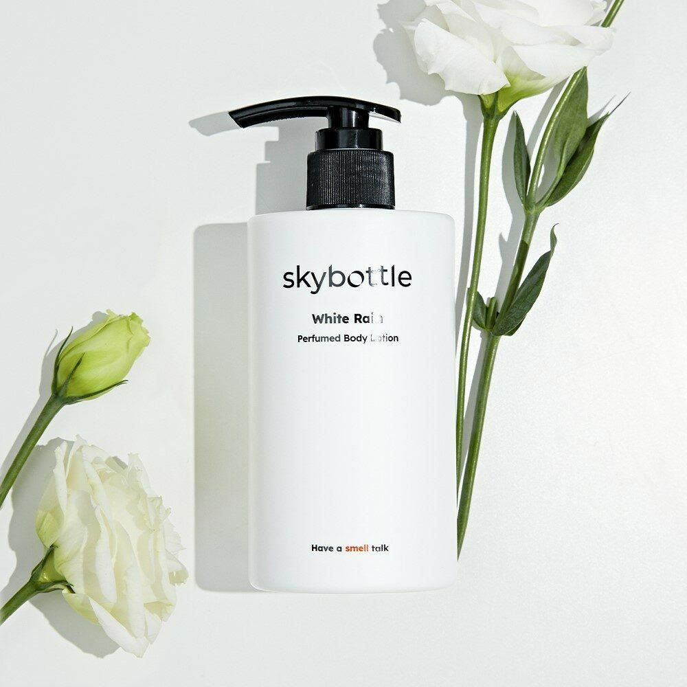 Witte SKYBOTTLE bodylotion fles met zwarte pomp, omringd door witte bloemen en knoppen.