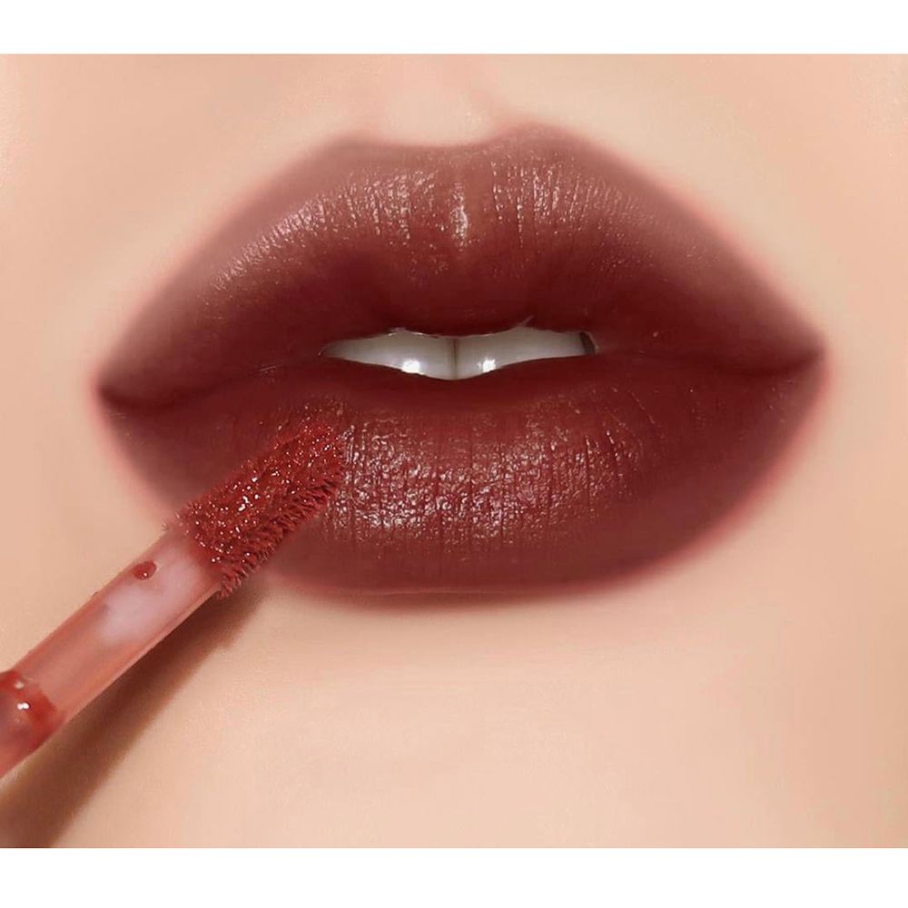 Lèvres avec gloss appliqué. Applicateur visible. Teinte rouge foncé.