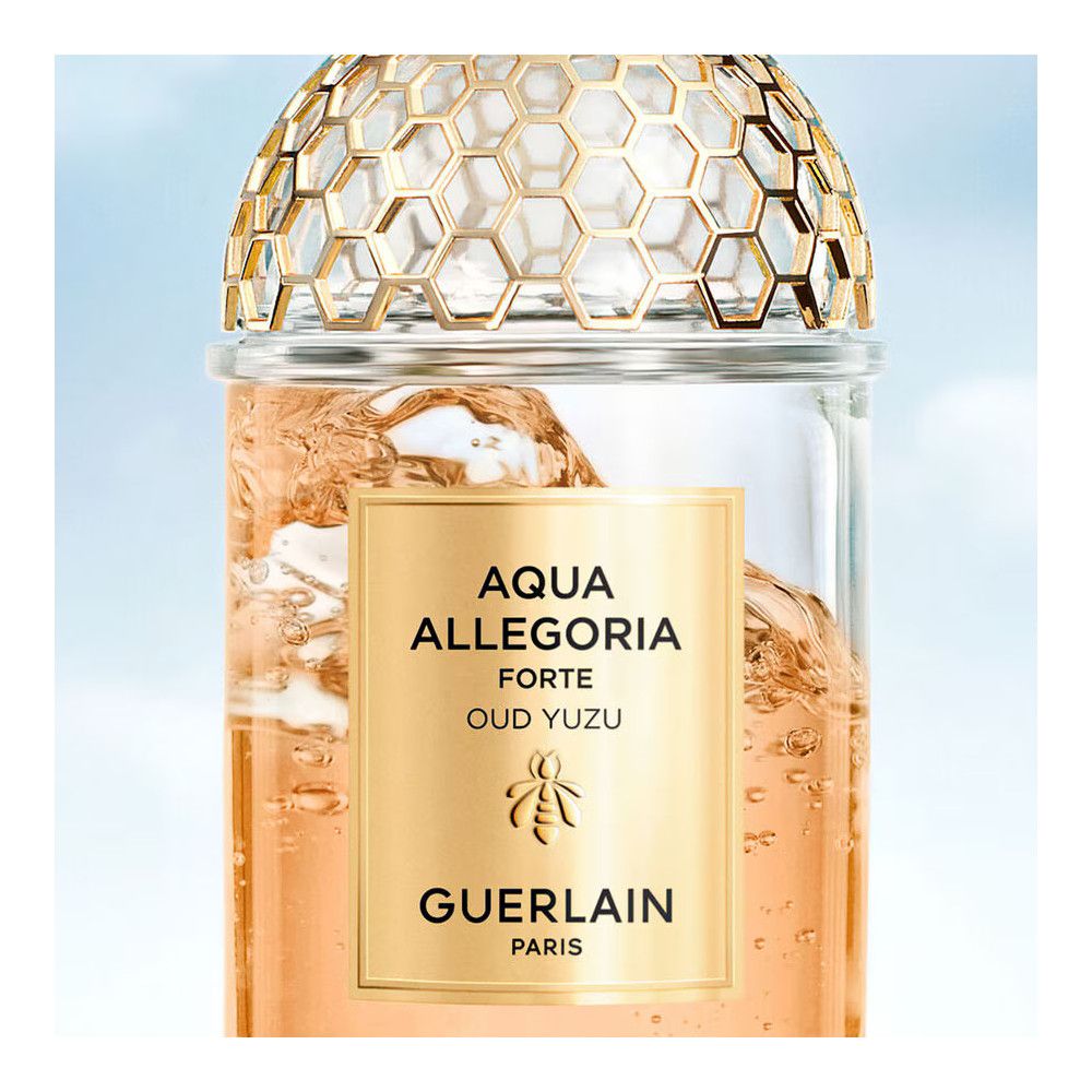 Glazen fles met gouden etiket. Tekst: AQUA ALLEGORIA FORTE OUD YUZU, Guerlain. Gouden honingraatpatroon op de dop.