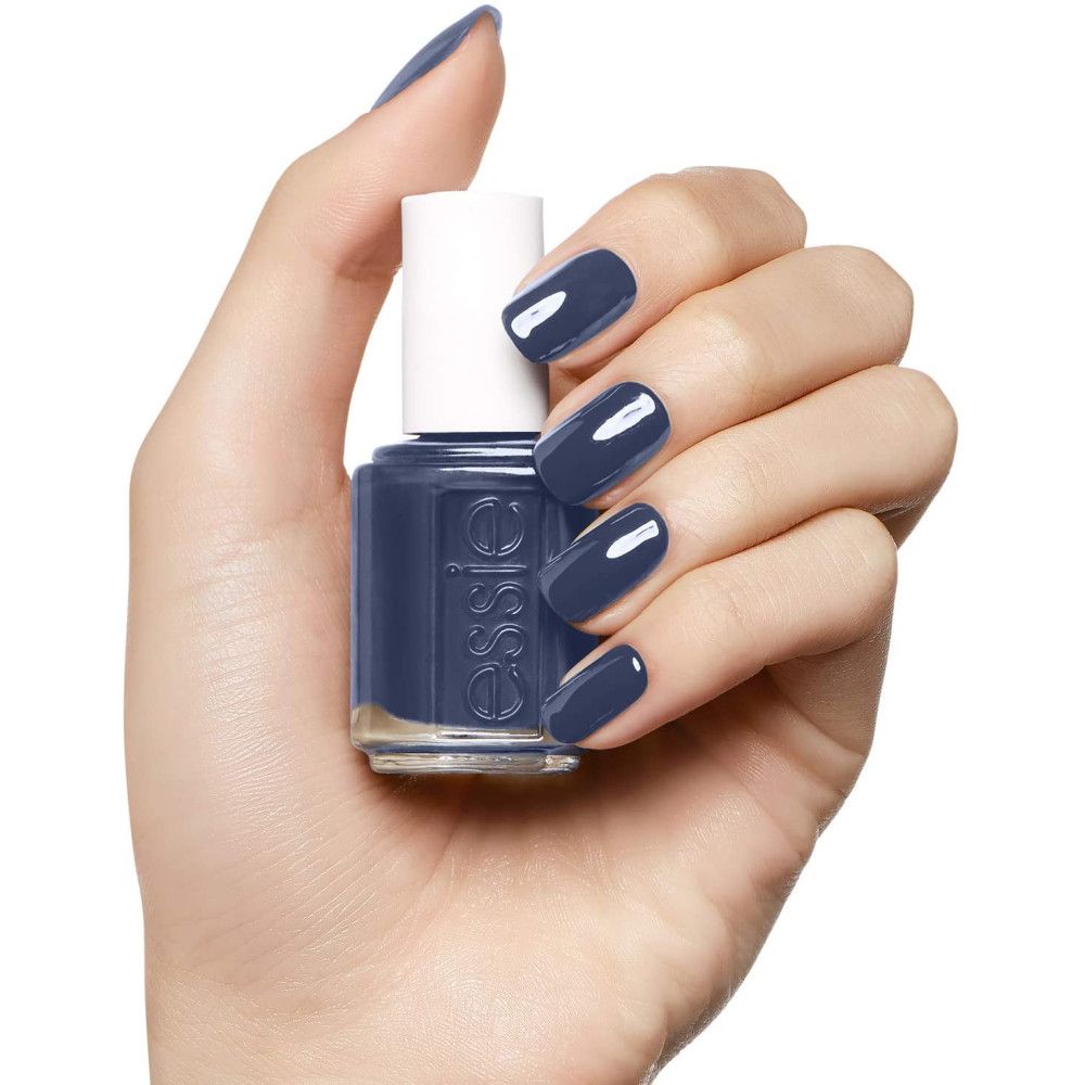 Essie nagellakflesje, donkerblauw. Flesje in hand, nagels gelakt in dezelfde kleur.