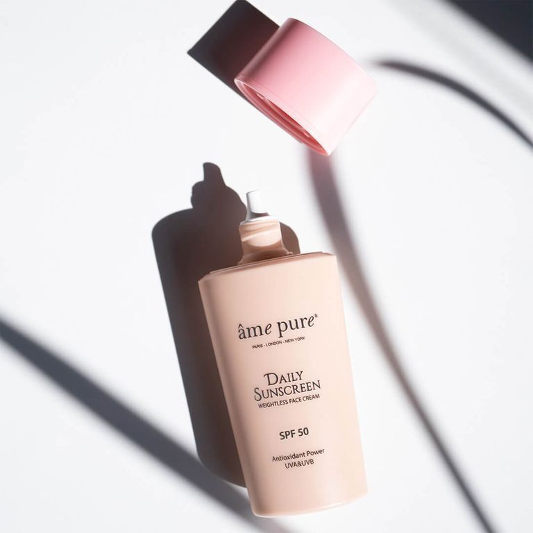 Un flacon de crème solaire SPF 50 avec bouchon rose ouvert, posé à l'ombre.