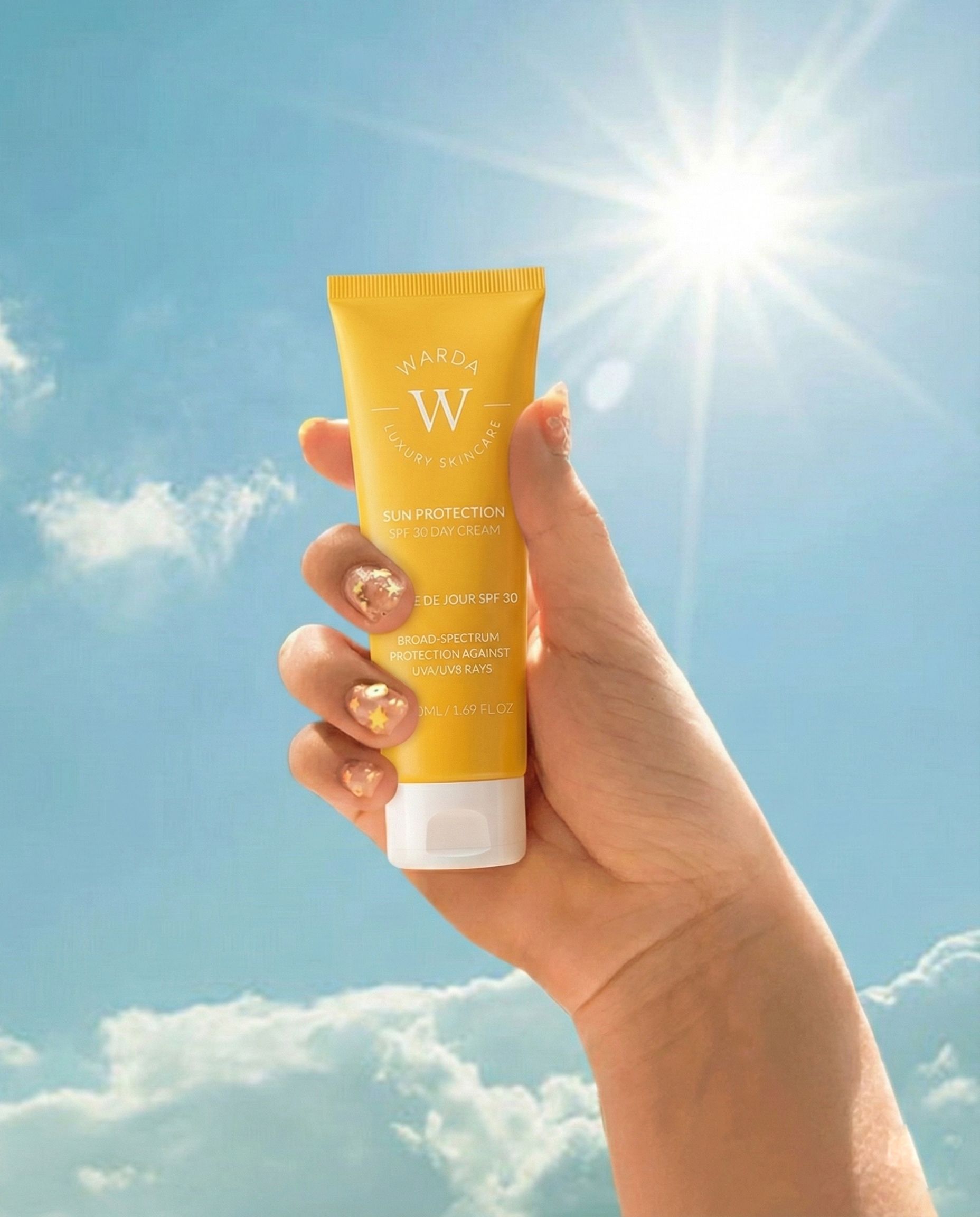 Gele tube in hand, voor blauwe hemel en zon. Opschrift: Sun Protection SPF 30 Day Cream. Merk: Warda.