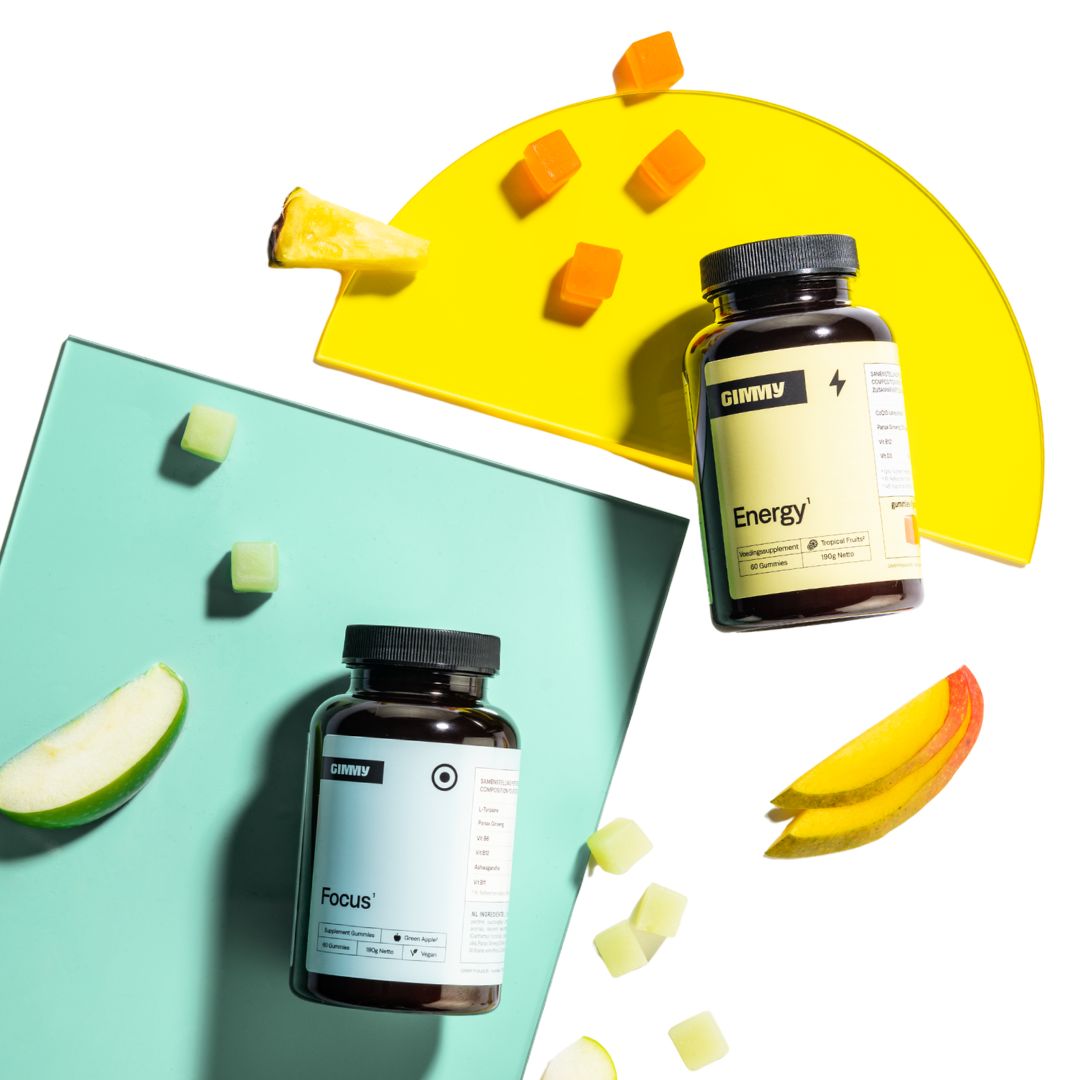 Twee flessen met zwarte doppen. Eén met geel etiket, "Energy", de andere met wit etiket, "Focus". Gele en groene gummies. Fruit.