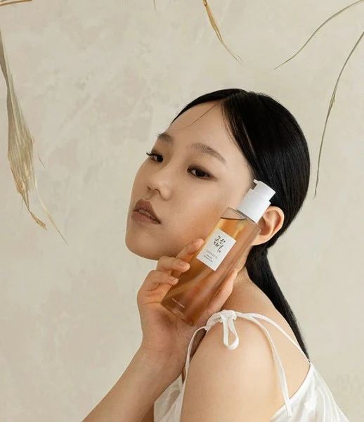 Een vrouw houdt een fles Beauty of Joseon Revive Serum tegen haar wang.