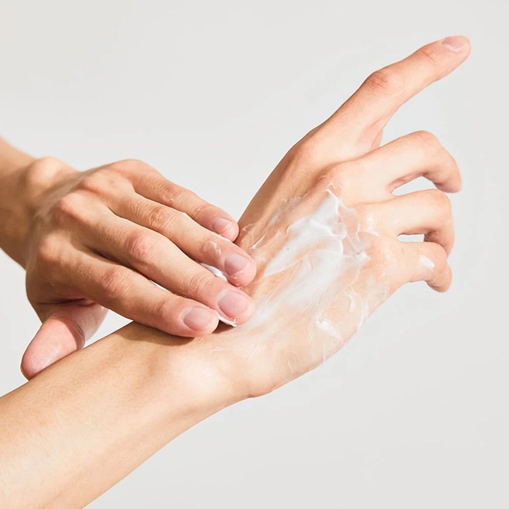 Mains appliquant de la crème sur la peau. Crème blanche sur la main. Fond clair.
