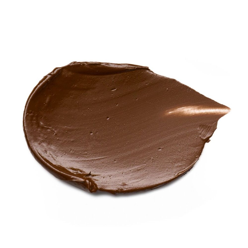 Tache de fond de teint marron sur fond blanc. Texture crémeuse, forme arrondie.