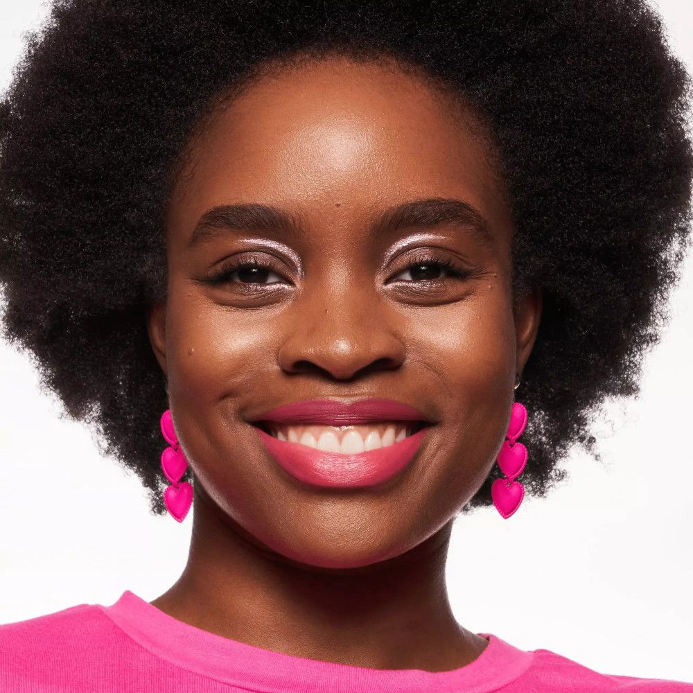 Portrait d'une femme à la peau foncée avec du rouge à lèvres rose. Elle porte des boucles d'oreilles roses et un haut rose.