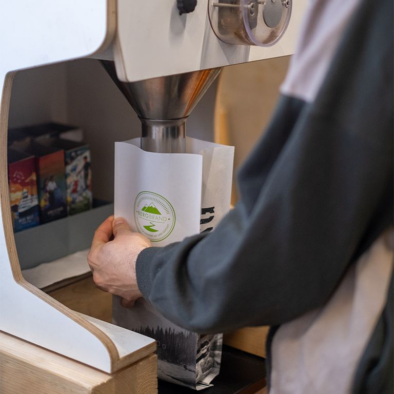 Personne remplit un paquet de grains de café. Paquet avec logo. Autres paquets en arrière-plan.