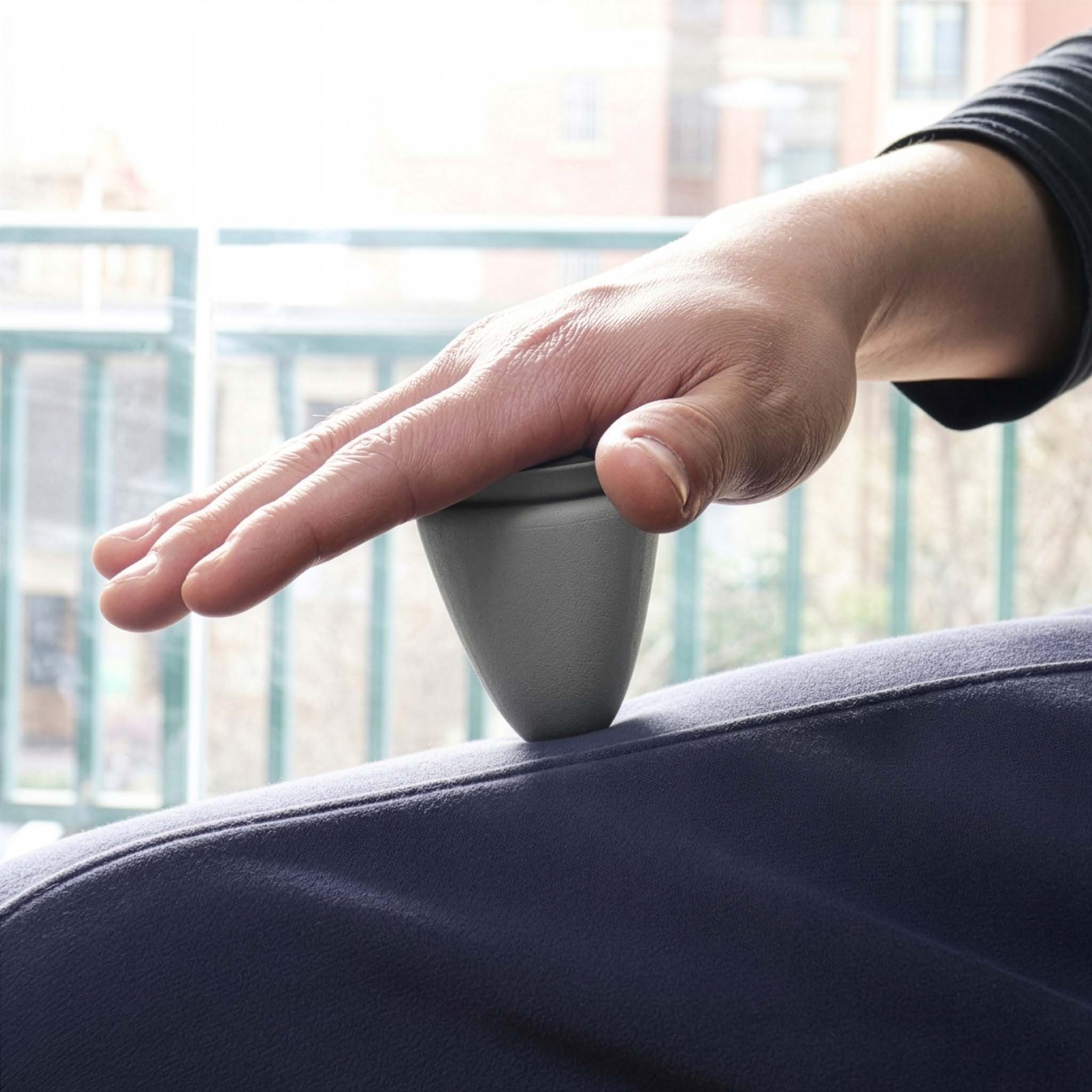 Grijs, kegelvormig product geplaatst op de dij van een persoon. Hand op het product.