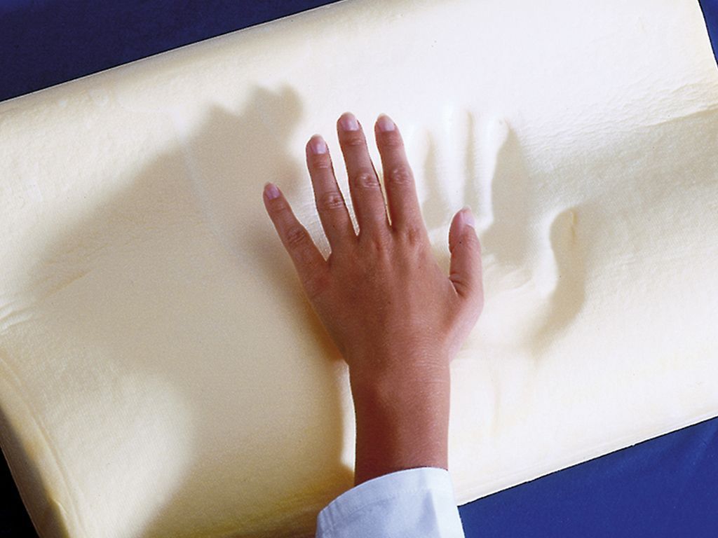 Oreiller beige, ergonomique. Main appuyant sur le matériau. Gros plan.