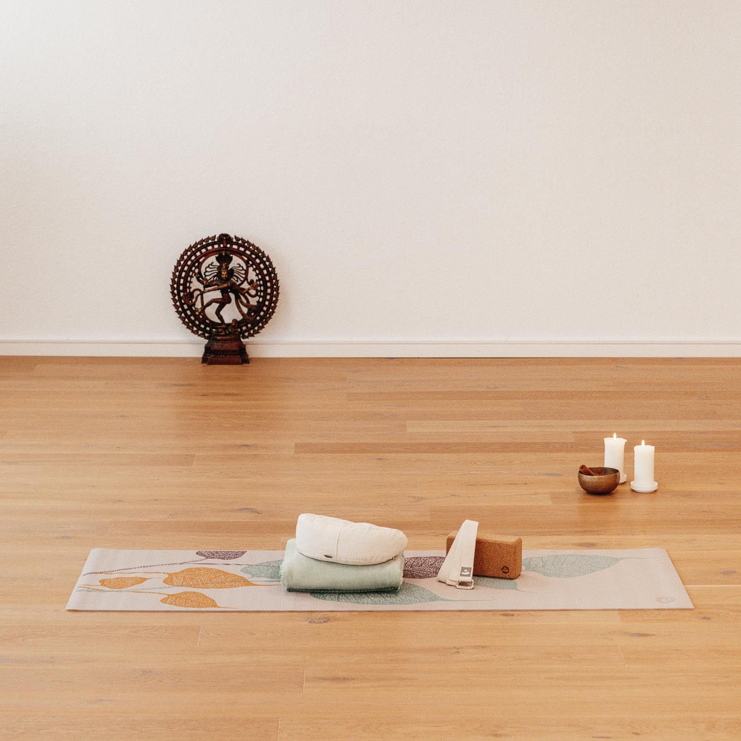 Yogamat met bladerenpatroon, omringd door yoga-accessoires: handdoek, blokken, kaarsen en beeldje.