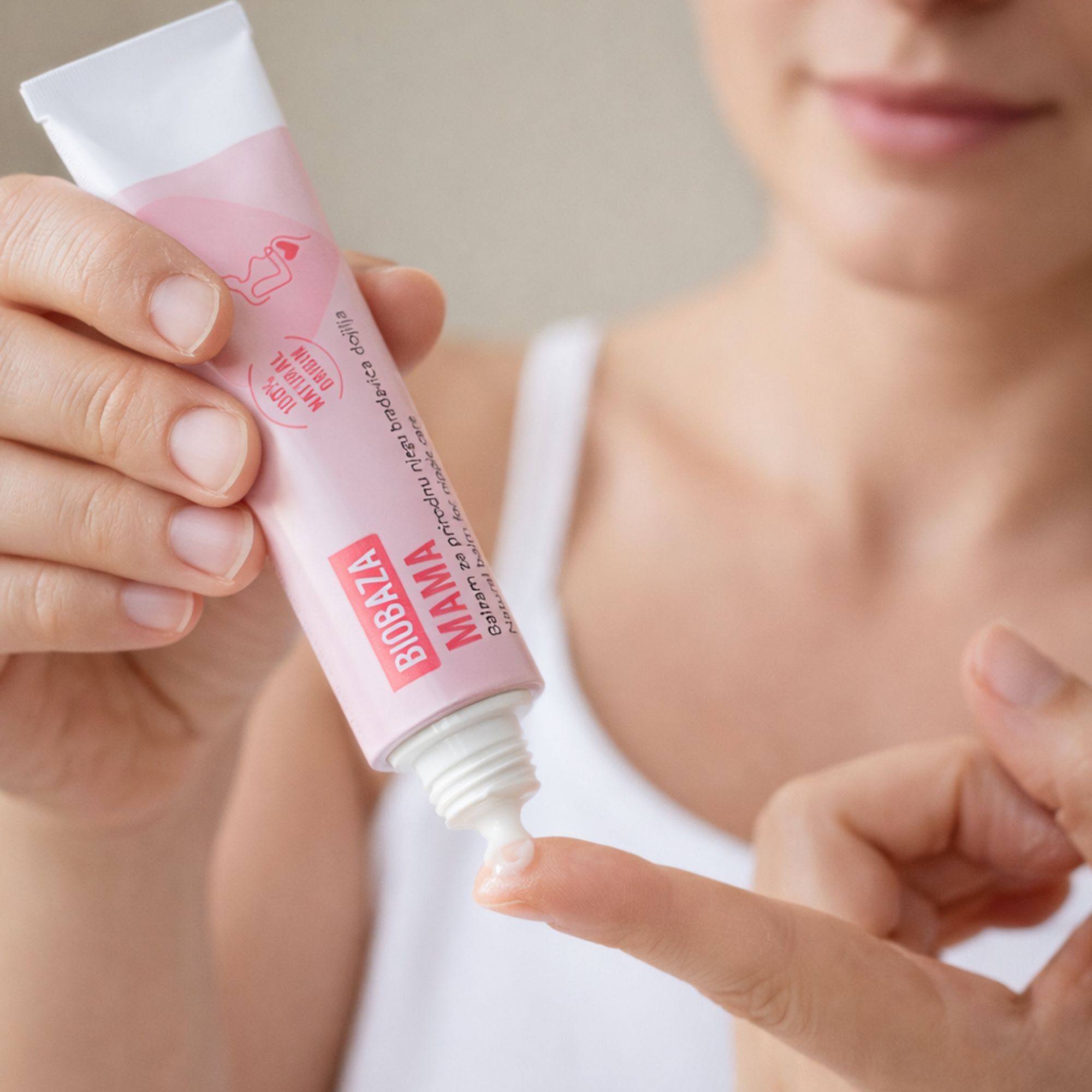 Roze tube met witte dop. Tekst: Biobaza Mama, tepelzalf. Product aangebracht op een vinger.