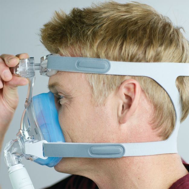 Vue latérale : homme ajustant le masque CPAP Philips Amara SE Gel Full.