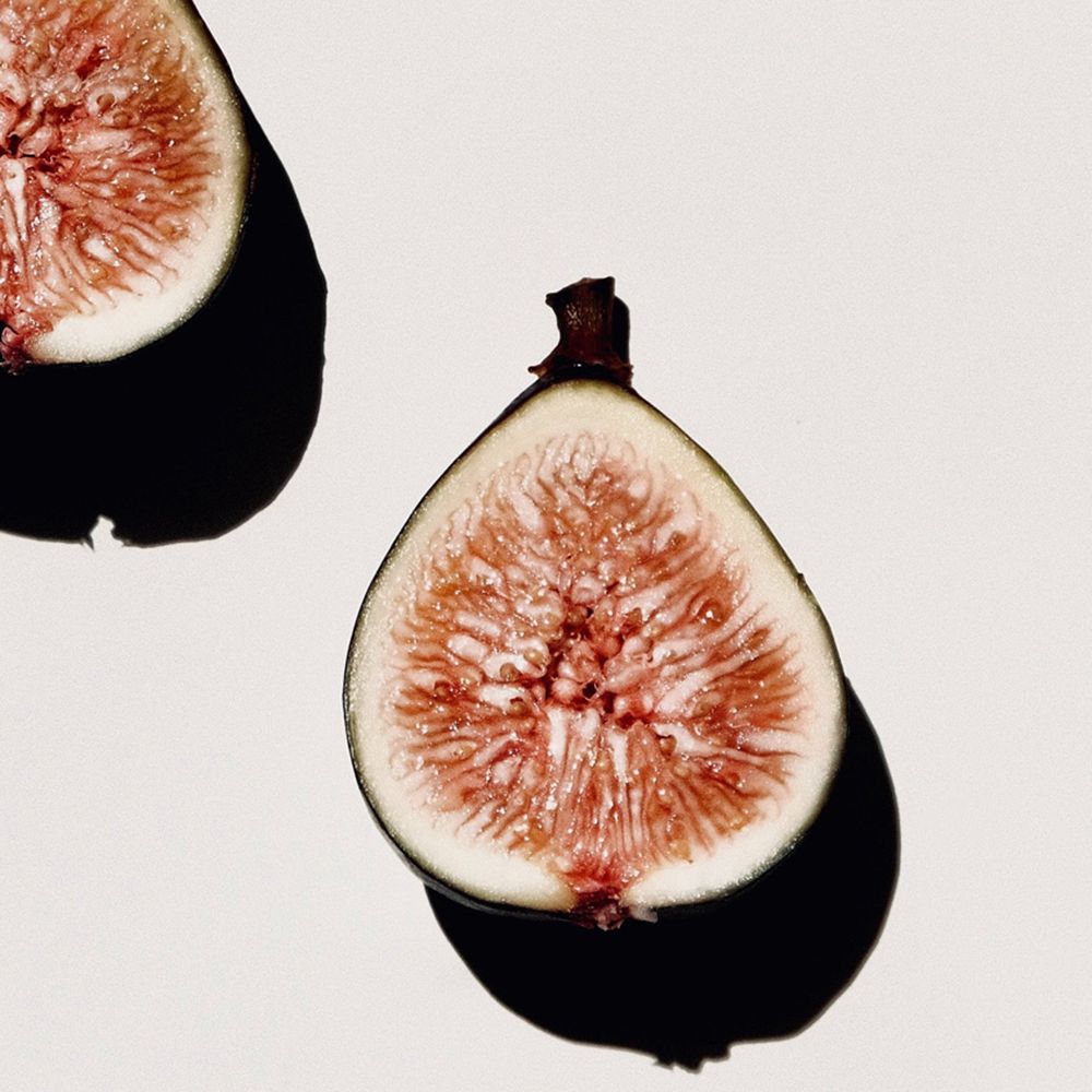 Deux figues coupées en deux sur fond blanc. Les figues sont rose clair et ont une ombre foncée.