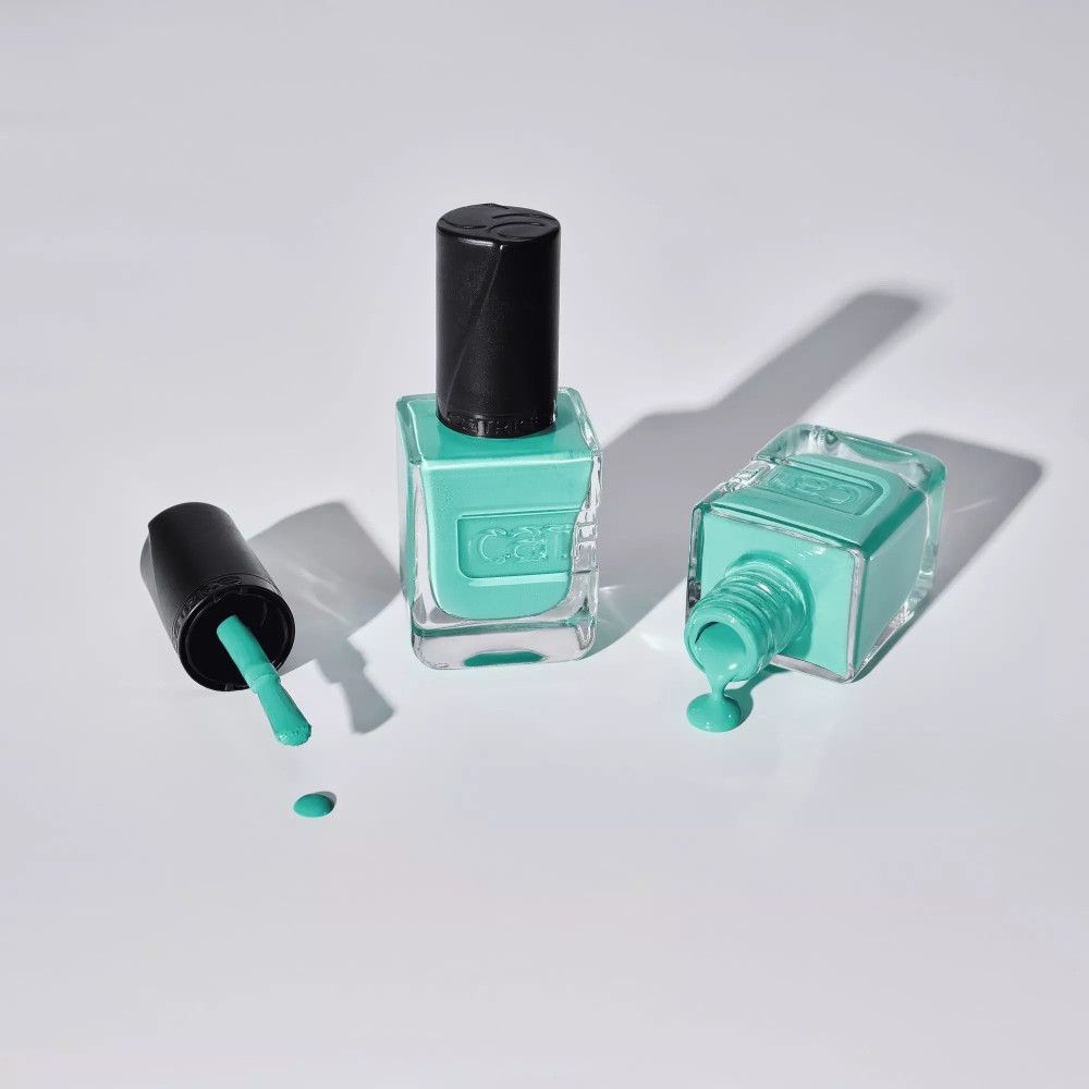 Trois flacons de vernis à ongles turquoise. Un avec le bouchon ouvert, un renversé, un debout.