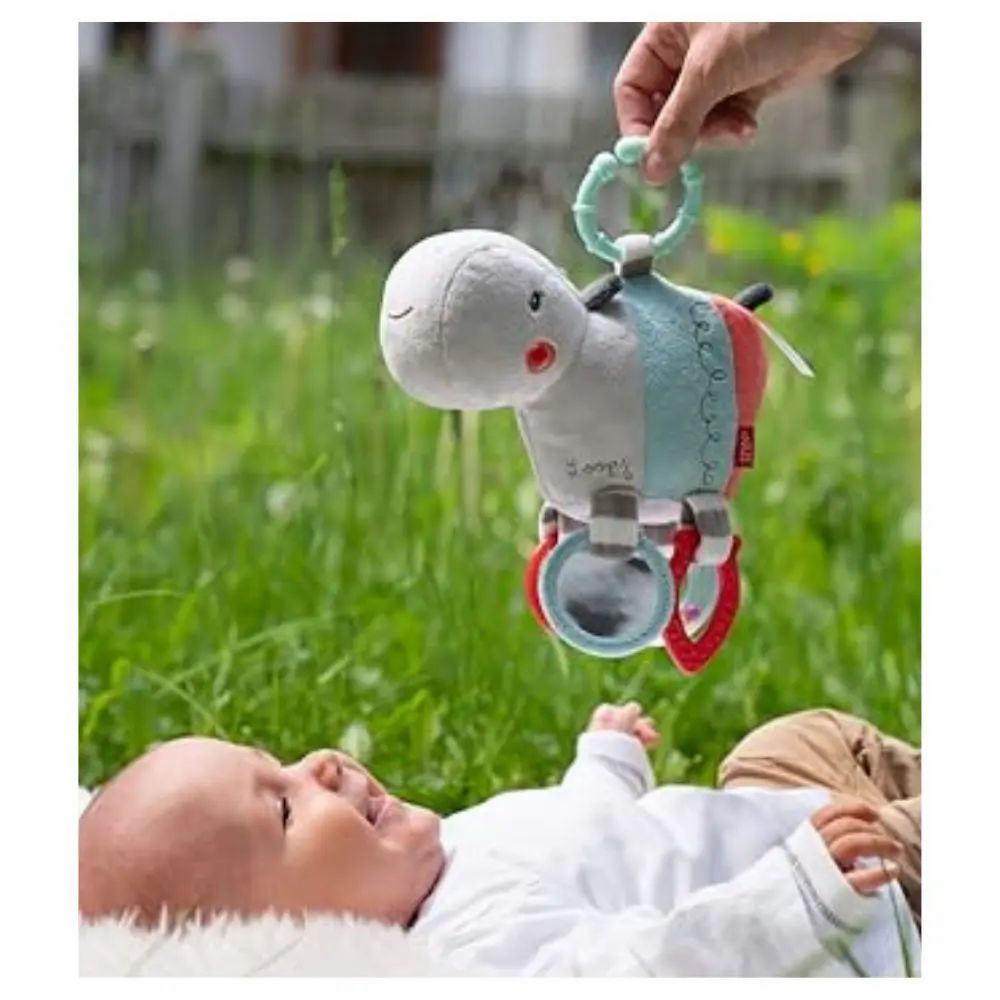 Bébé sur l'herbe, main tenant une peluche hippopotame. Jouet avec miroir et anneaux. Bébé regarde.