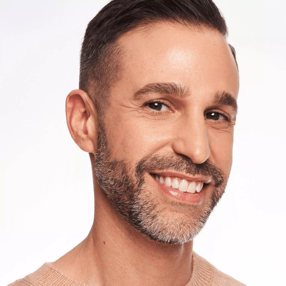 Portret van een man met baard. Hij glimlacht. Hij draagt een beige top.