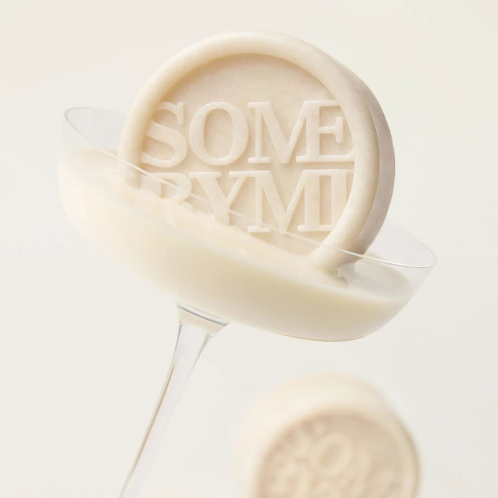 Un savon rond avec le texte SOME BYMI dans un verre contenant du liquide.