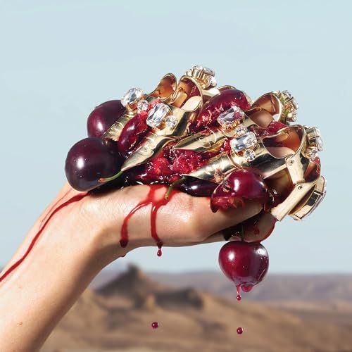 Hand met gouden ringen met edelstenen, houdt pruimen vast. Rood sap druppelt. Achtergrond: landschap.