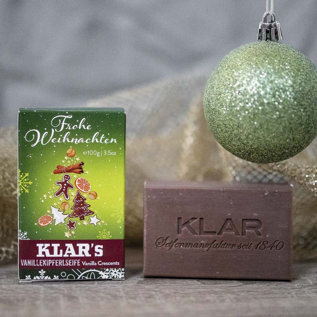 Emballage et savon. Emballage avec motif sapin de Noël. Savon avec "KLAR" estampillé. Boule de Noël en arrière-plan.