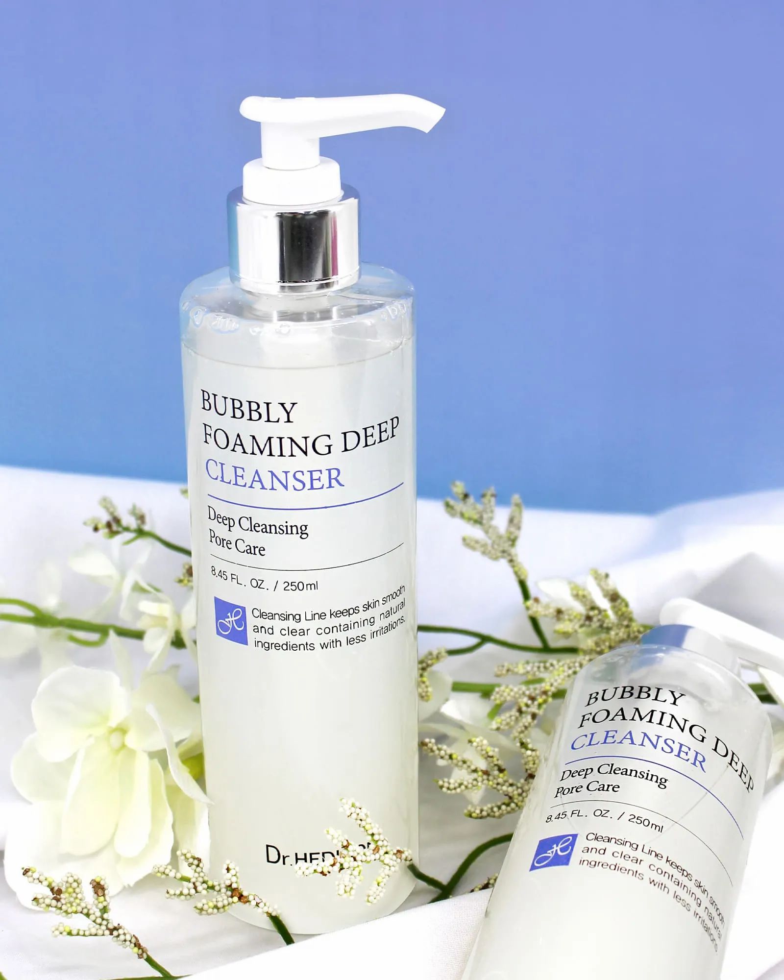 Deux flacons avec pompe. Inscription : Bubbly Foaming Deep Cleanser. Marque : Dr. Hedison. Sur tissu blanc.