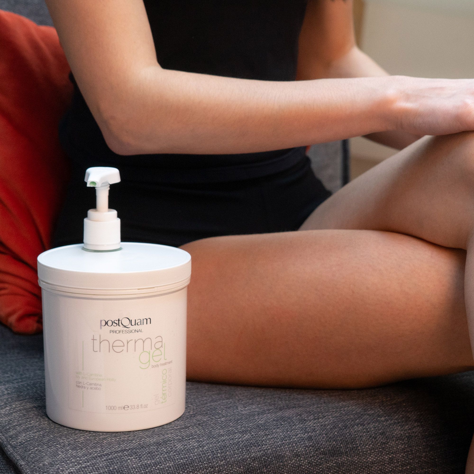 Vrouw zit met witte pot 'PostQuam therma gel'. Pomp op pot. Draagt zwart topje.