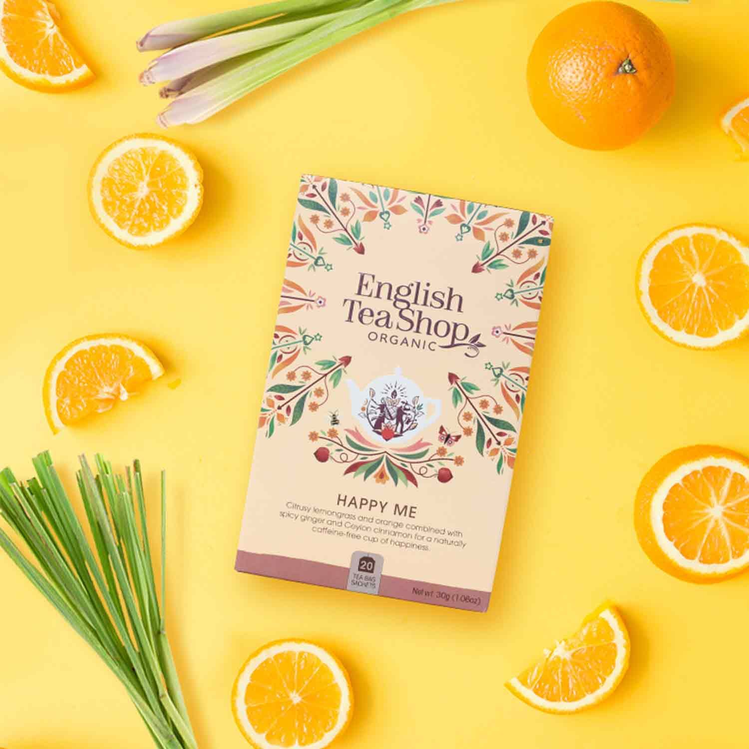Doosje ETS - Happy Me wellness-thee bio op gele achtergrond met sinaasappels en citroengras. Opschrift: English Tea Shop Organic, Happy Me.