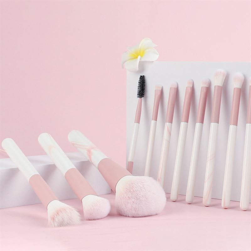 Ensemble de pinceaux de maquillage. Pinceaux avec manches roses et blancs. Différentes formes et tailles. Placé sur une surface rose. Certains pinceaux sont dressés.