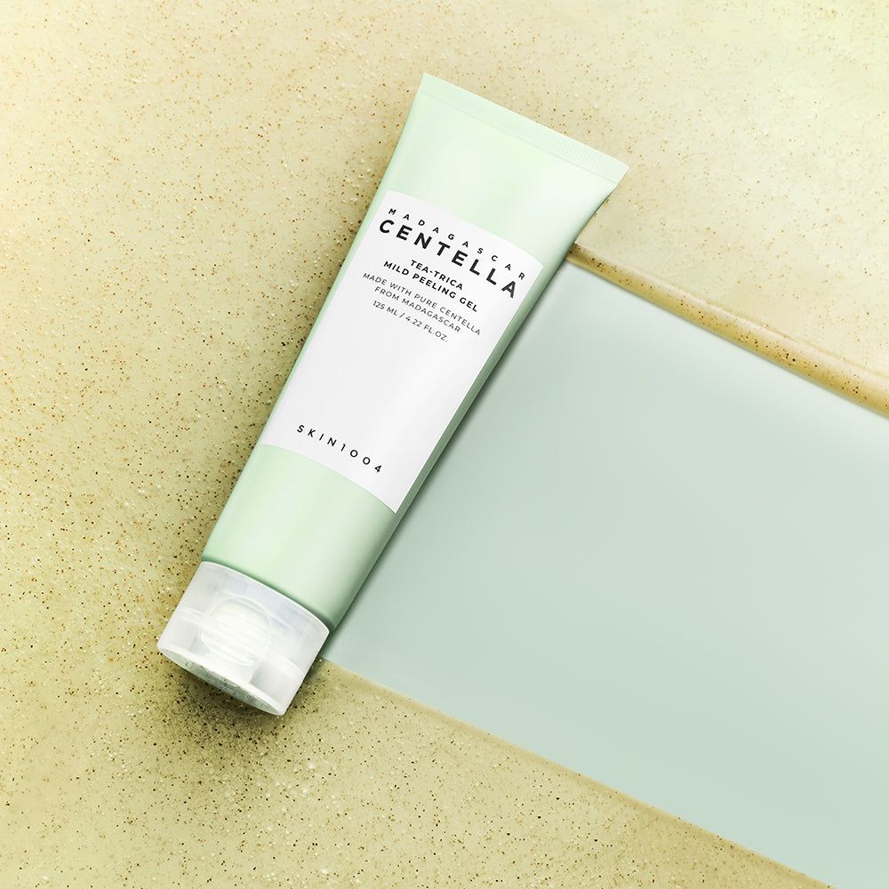 Groene tube met wit etiket. Opschrift: MADAGASCAR CENTELLA, Tea-Trica Mild Peeling Gel. Ligt op oppervlak.
