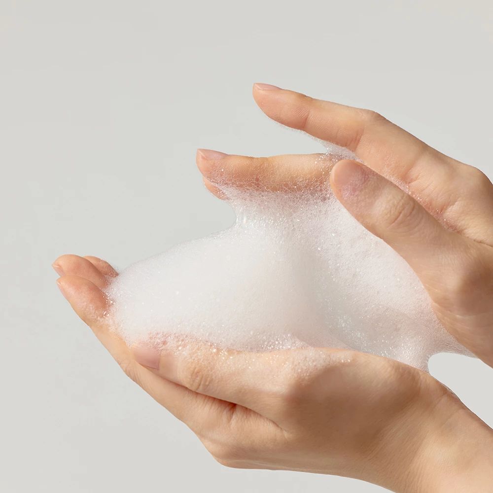 Handen houden witte schuim vast. Schuim is dicht en luchtig. Lichte huid. Achtergrond is lichtgrijs.