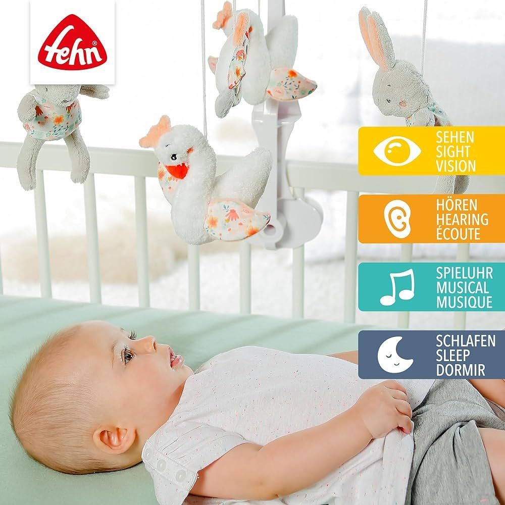 Bébé sous mobile. Mobile avec lapins, cygnes et miroir. Logo Fehn. Pictogrammes pour voir, entendre, boîte à musique, dormir.