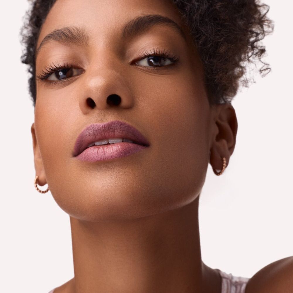 Portret van een vrouw met roze lippenstift. Ze draagt oorbellen. De achtergrond is licht.