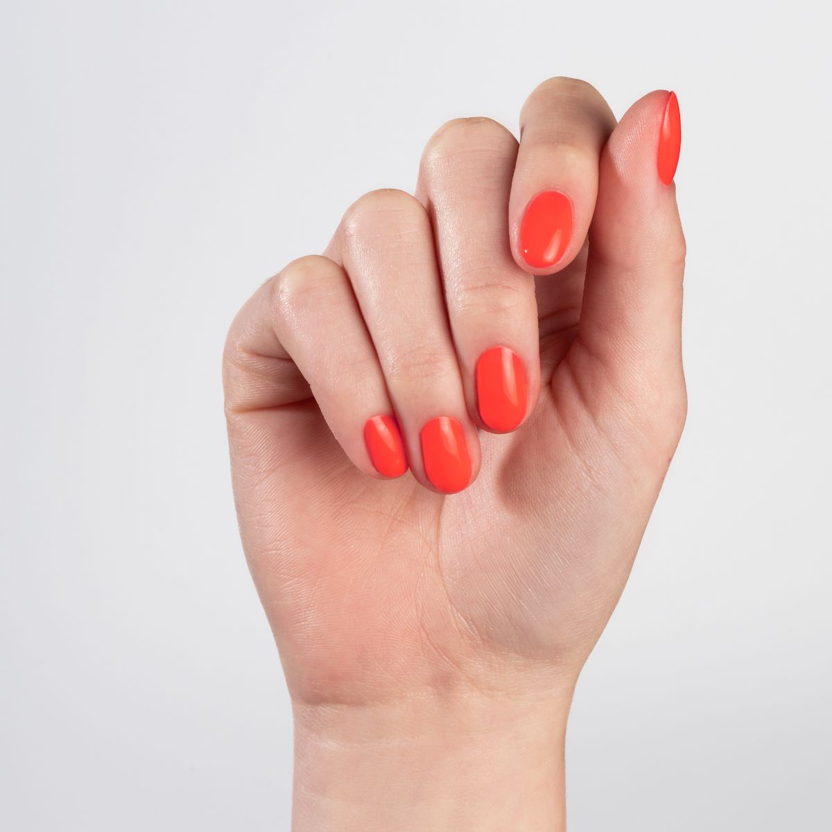 Main avec des ongles peints en orange. La main est présentée sur un fond blanc.
