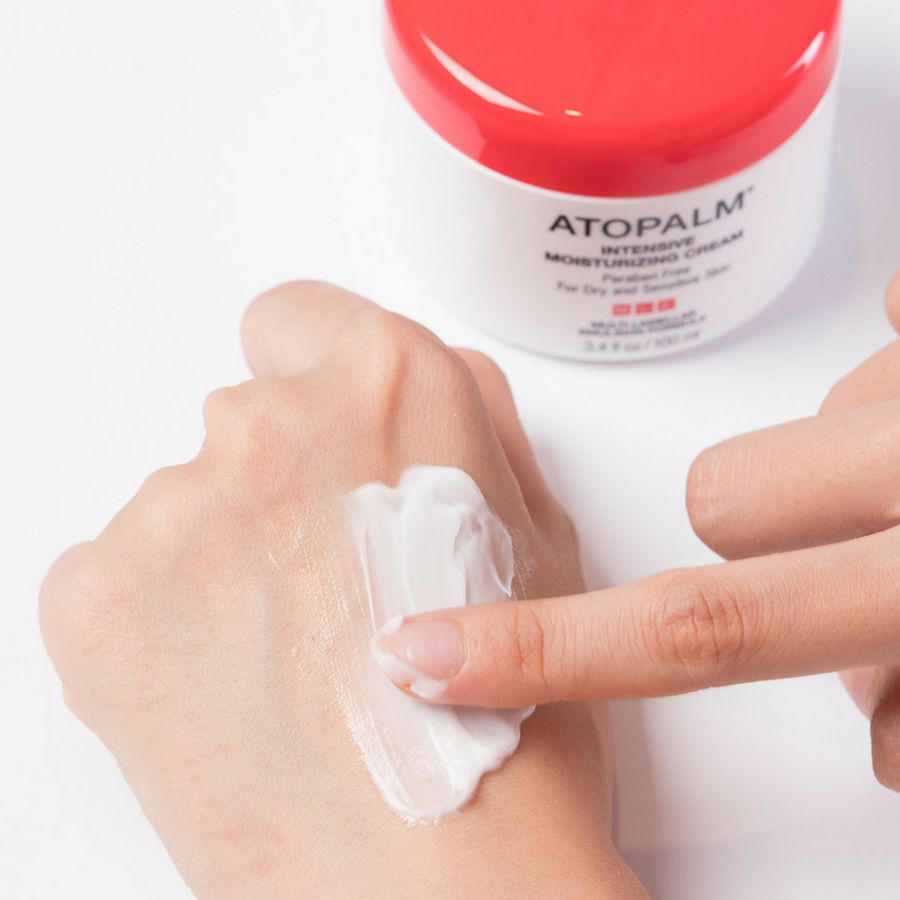 Hand met crème. Opschrift: ATOPALM INTENSIVE MOISTURIZING CREAM. Crème op hand aangebracht. Voor droge en gevoelige huid.