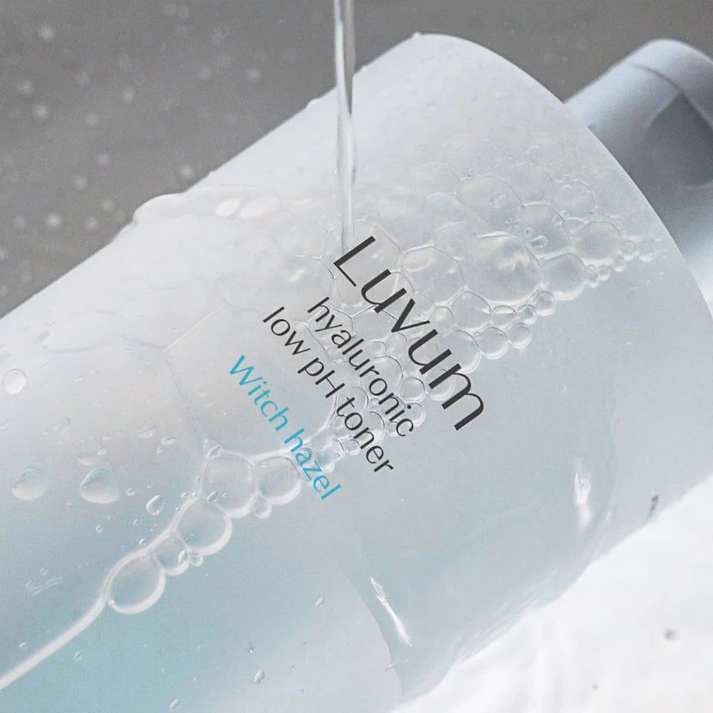Liquide clair coulant sur une bouteille. La bouteille porte l'inscription "Luvum hyaluronic low pH toner Witch hazel".