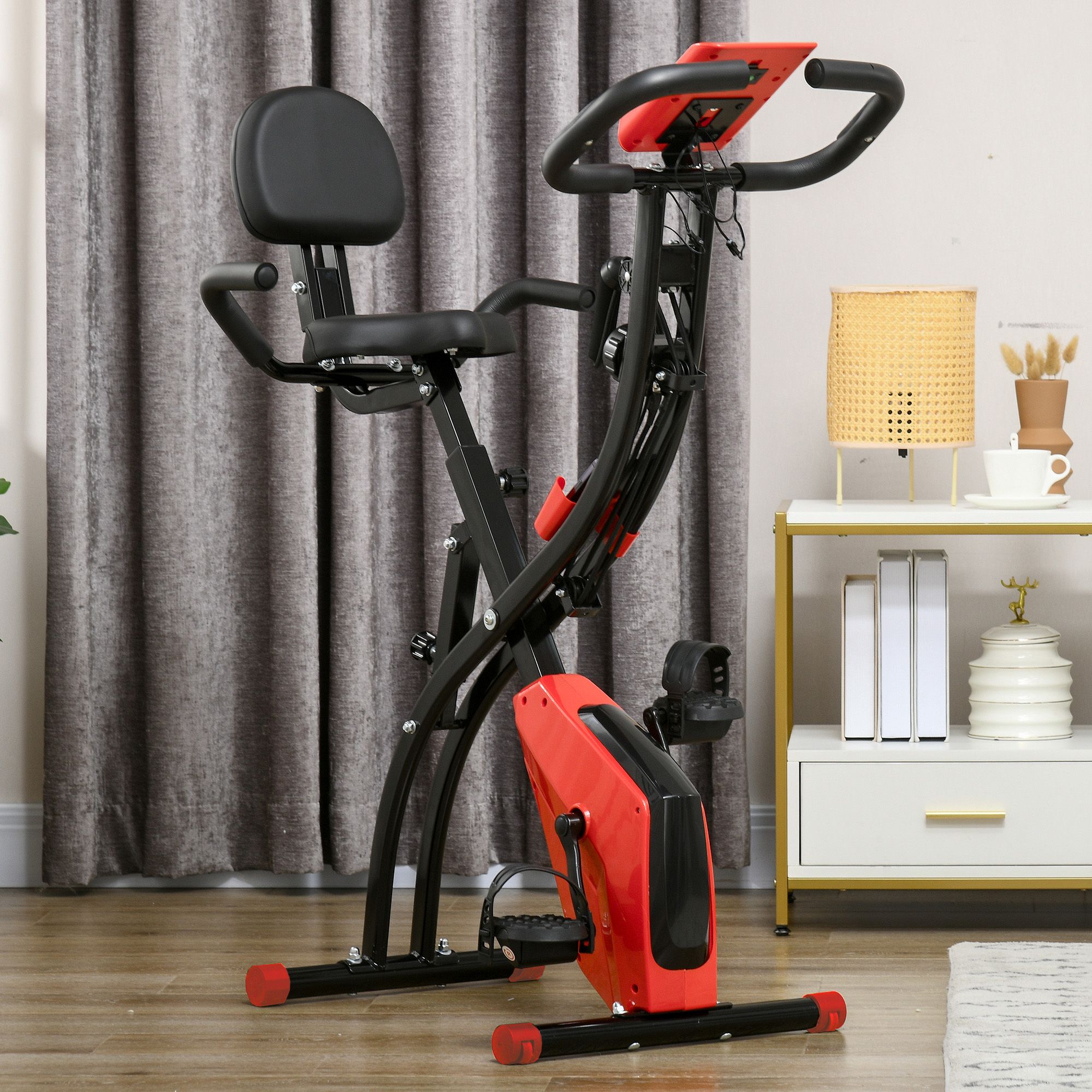 Rode en zwarte hometrainer in een woonkamer. Met zitting, rugleuning, pedalen en stuur. Zwarte handgrepen, rood bedieningspaneel.